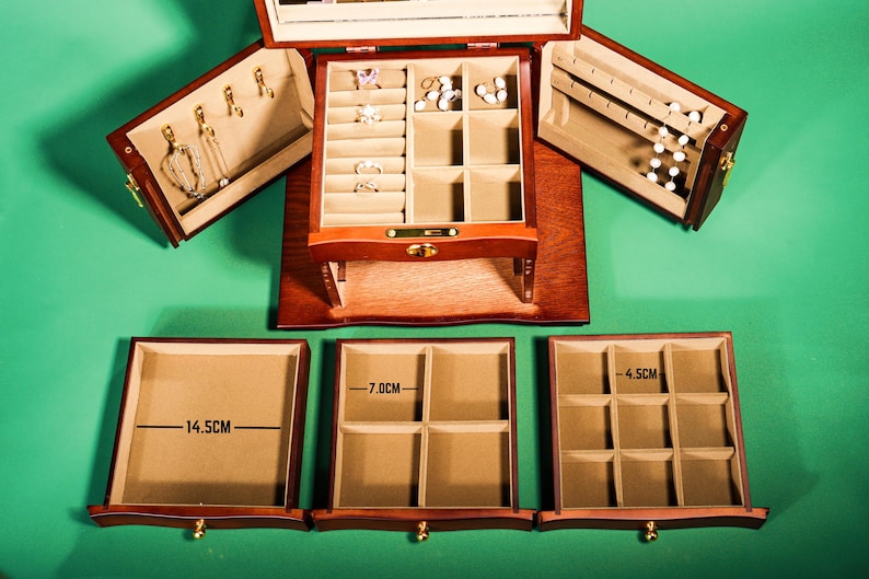 May include: A wooden jewelry box with three drawers. The top drawer has a mirror and compartments for rings and earrings. The bottom two drawers have compartments for necklaces and bracelets. The drawers are labeled with measurements in centimeters: 14.5 cm, 7.0 cm, and 4.5 cm.