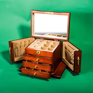May include: A wooden jewelry box with a mirrored lid, three drawers, and a compartment for hanging necklaces. The box is open, revealing the interior compartments and drawers.