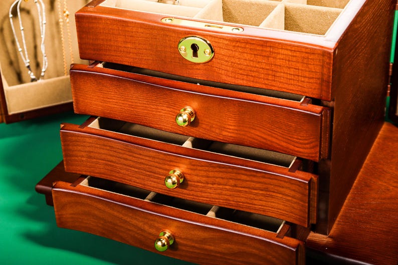 May include: A wooden jewelry box with four drawers and a hinged top. The box has a gold-colored lock and keyhole. The drawers have gold-colored knobs.