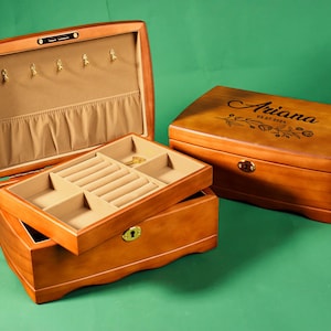 Könnte beinhalten: Eine Holzkästchen für Schmuck mit einem Scharnierdeckel und einem Fach für Ringe und Ohrringe. Die Box ist mit dem Namen "Ariana" und dem Datum "03.27.2004" graviert.