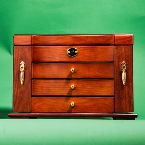 May include: A wooden jewelry box with a dark brown finish and gold accents. The box has four drawers and a keyhole.