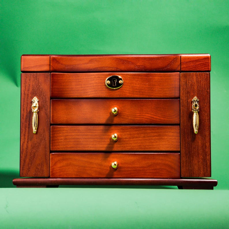 May include: A wooden jewelry box with a dark brown finish and gold accents. The box has four drawers and a keyhole.