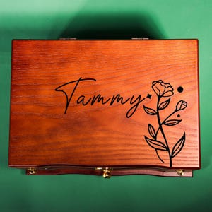 May include: A wooden box with a floral design and the name "Tammy" engraved on the top. The box has a hinged lid and a small drawer.