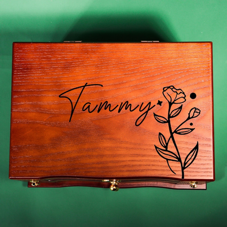 May include: A wooden box with a floral design and the name "Tammy" engraved on the top. The box has a hinged lid and a small drawer.
