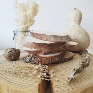 Puede incluir: Una pila de cuatro rodajas de madera, cada una con un borde de corteza natural, se asienta sobre un tronco de madera grande. Las rodajas están dispuestas en un patrón escalonado, creando un aspecto rústico y orgánico. También se incluyen flores secas y una calabaza en la imagen.