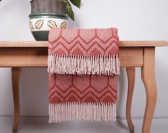 Puede incluir: Una manta de tiro de color rojo y blanco con flecos sobre una mesa de madera. La manta está doblada por la mitad y tiene un diseño geométrico.