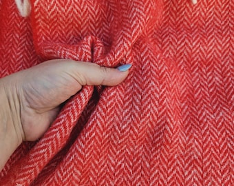 May include: Red and white herringbone patterned blanket with a hand holding a corner of the blanket.
