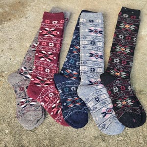 May include: Five pairs of knee-high socks with geometric patterns. The socks feature a variety of colors, including gray, burgundy, navy blue, and black. Each sock has a unique design with diamond and zigzag patterns.