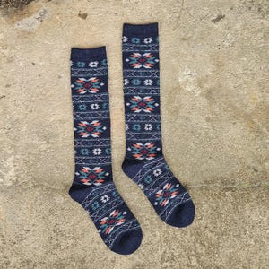 Può includere: Un paio di calzini al ginocchio blu navy con un motivo geometrico in verde acqua, arancione e bianco. I calzini sono realizzati in un materiale morbido e sono progettati per il comfort e il calore. Il motivo si ripete lungo tutta la lunghezza.