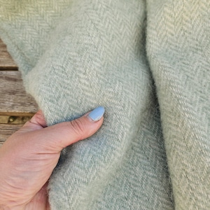 以下が含まれることがあります： ヘリンボーン柄の柔らかく薄い緑色の毛布。毛布はふわふわした素材で、上品な光沢があります。