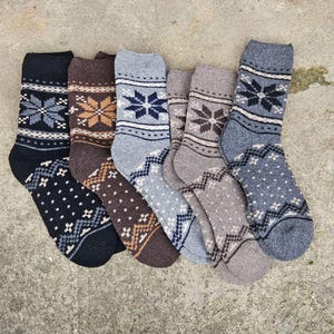 May include: Six pairs of warm winter socks in various shades of gray, brown, and black. Each sock features a snowflake and geometric pattern in contrasting colors. The socks are made of a thick, knitted material.