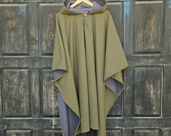 May include: A hooded poncho with a green outer layer and a grey fleece lining. The poncho is hanging on a wooden hanger against a dark wooden background.