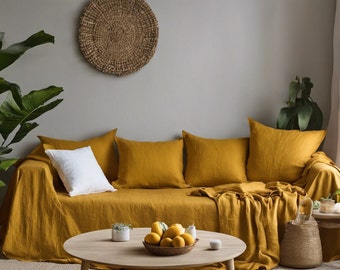 May include: A mustard yellow linen sofa with three throw pillows and a throw blanket. The sofa is in a living room with a woven wall hanging, a potted plant, and a coffee table with a bowl of lemons.