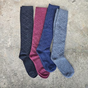 May include: Four knee-high socks in shades of navy, burgundy, blue, and gray, each with a diamond pattern. The socks are displayed on a concrete surface, showcasing their colors and design. These socks are suitable for various outfits.