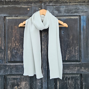 May include: A light grey knitted scarf hanging on a wooden hanger against a dark wood background.