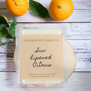 May include: A white soy wax melt in a clear plastic container with a brown label that reads "GOLDEN POPPY CANDLE CO. Sun Ripened Citrus 3OZ/85G 6CT SOY WAX MELTS MADE IN RED BLUFF, CA"