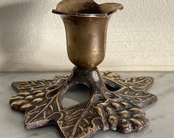 Puede incluir: Un candelero de latón con una base en forma de hoja y un portavelas en forma de campana.