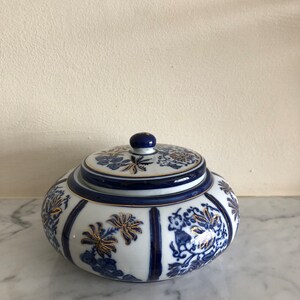 May include: A white porcelain jar with a blue and gold floral design. The jar has a lid and is decorated with a traditional Chinese pattern.