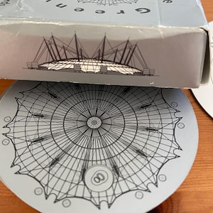 Könnte beinhalten: Eine graue Spielkartenbox und ein Untersetzer mit dem Greenwich Dome in London. Auf der Box steht "Greenwich Dome London". Der Untersetzer zeigt eine Grafik des Doms und die Zahl acht.