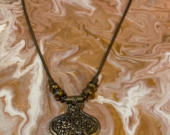 May include: A gold necklace with a detailed pendant featuring a swirling design. The chain is made of small, round beads.