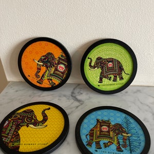 May include: Four round coasters with black frames and colorful designs featuring elephants with intricate patterns. Each coaster has the text "The Bombay Store" printed on the bottom.