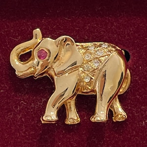 May include: A gold-tone elephant brooch with a red rhinestone eye and clear rhinestones on the body.