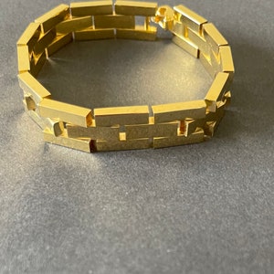 May include: A gold-toned bracelet with a linked chain design. The links are rectangular and interlock to form a continuous band.