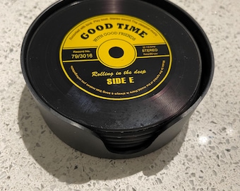 May include: A set of black vinyl record coasters with yellow and white labels. The labels read "GOOD TIME WITH GOOD FRIENDS" and "Rolling in the deep SIDE E". The coasters are stacked in a black holder.