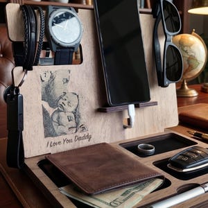 Peut inclure: Organisateur de bureau en bois avec compartiments pour téléphone, montre, lunettes de soleil, portefeuille, clés et photo avec le texte "I Love You Daddy". Comprend une montre noire, des lunettes de soleil noires et un portefeuille en cuir marron.