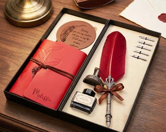 Könnte beinhalten: Ein Kalligraphie-Set im Vintage-Stil in einer schwarzen Box. Das Set enthält eine rote Federkiel, Tinte, ein rotes Notizbuch mit dem Namen "Melissa" und einen runden Untersetzer mit Federdesign und Text.