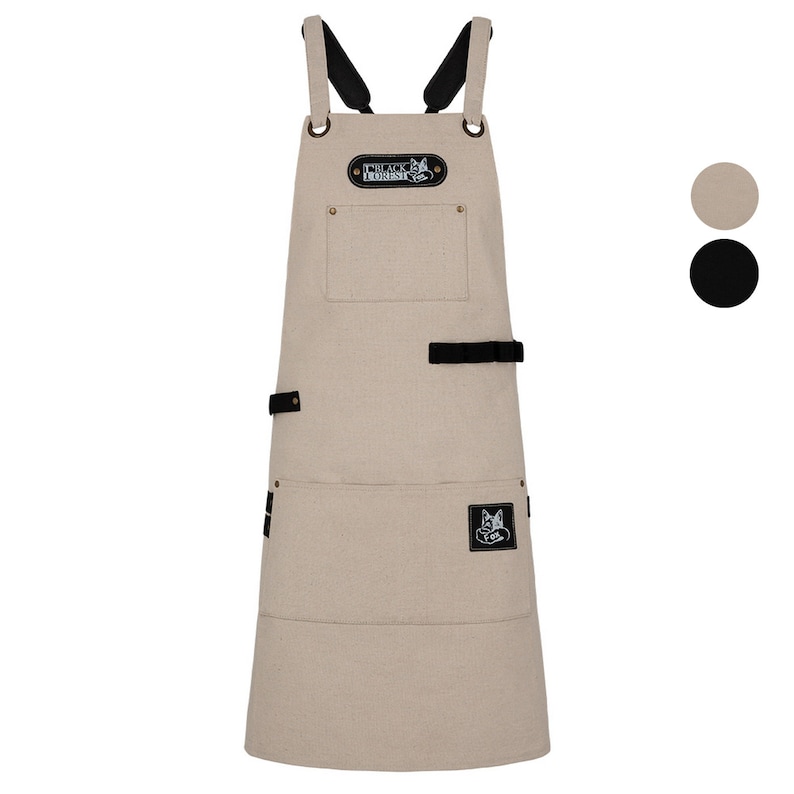 May include: A beige canvas apron with black straps and a black leather patch with the text "Black Forest" and a wolf logo. The apron has two large pockets and a smaller pocket on the front.