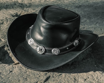 May include: A black leather cowboy hat with a silver band and decorative accents. The hat has a wide brim and a tall crown.