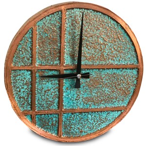 Puede incluir: Un reloj redondo de color cobre con una esfera azul turquesa. La esfera del reloj está dividida en cuadrados con un patrón de cuadrícula negra. El reloj tiene agujas negras.