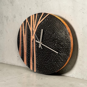 Peut inclure: Une horloge murale ronde avec un cadran noir et des accents cuivrés. L'horloge présente un motif d'arbre sur le côté gauche et une surface texturée. Les aiguilles de l'horloge sont argentées.