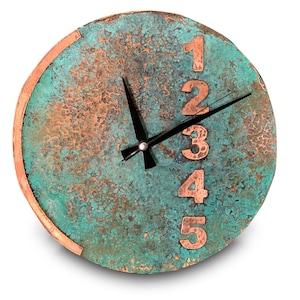 Puede incluir: Un reloj redondo de tono cobre con un acabado verde turquesa desgastado. La esfera del reloj tiene agujas negras y números de cobre del 1 al 5.