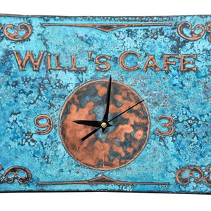 May include: A blue and copper clock with the words "Will's Cafe" on it. The clock face is copper with black hands and the numbers 3 and 9.