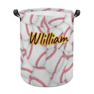 May include: A white laundry hamper with a baseball design. The hamper is covered in images of baseballs with red stitching. The name "William" is printed in yellow script with a black outline. The hamper has black handles.