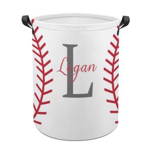 May include: White laundry hamper with red baseball stitching design and black handles. The hamper features a large gray letter "L" with the name "Logan" in a cursive font, perfect for a baseball fan.