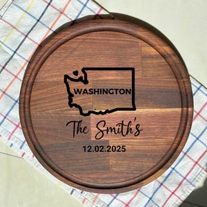 May include: A circular, dark brown wooden serving board with a carved edge. It displays a black outline of the Washington state map with "WASHINGTON" inside. Below is "The Smith's" and the date "12.02.2025".