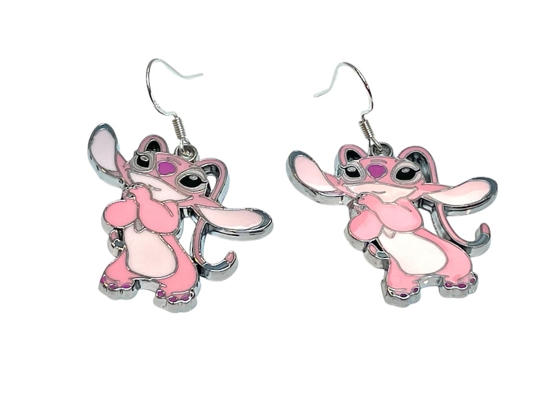 Puede incluir: Un par de pendientes de esmalte rosa y blanco con un dise&ntilde;o de personaje de dibujos animados. Los pendientes tienen un contorno de metal plateado y ganchos para las orejas. El personaje tiene ojos grandes y est&aacute; en una pose.