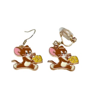 May include: A pair of cartoon-themed earrings featuring Jerry the mouse holding a piece of cheese. The earrings are brown, white, and yellow with pink accents. One earring has a hook, and the other has a clip-on backing.