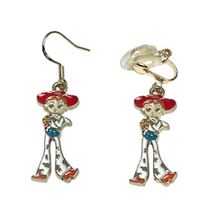 May include: A pair of gold-coloured earrings with a cartoon character design. One earring has a hook, the other a clip-on. Each earring depicts a character with a red hat, white trousers with black spots, and a blue top.