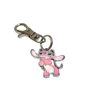 Puede incluir: Llavero de esmalte rosa y blanco con un personaje de dibujos animados con orejas grandes y un cierre de metal plateado. El personaje est&aacute; de pie con los brazos extendidos. Dise&ntilde;ado para llaves o bolsos.