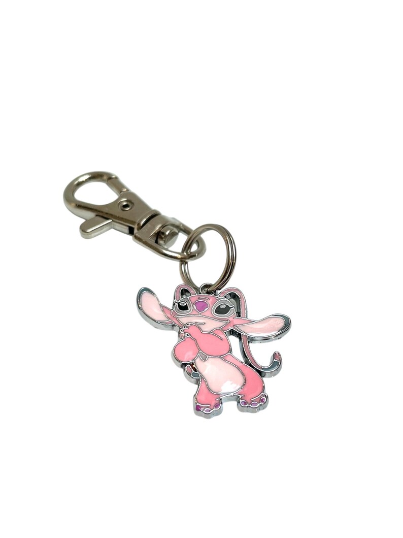 Puede incluir: Llavero de esmalte rosa y blanco con un personaje de dibujos animados con orejas grandes y un cierre de metal plateado. El personaje est&aacute; de pie con los brazos extendidos. Dise&ntilde;ado para llaves o bolsos.