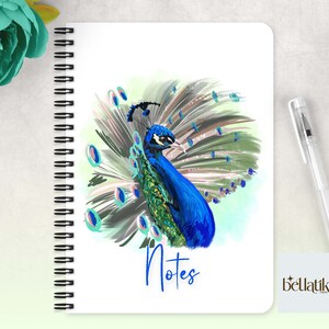 Peut inclure: Un carnet &agrave; spirales avec une couverture blanche illustrant un paon color&eacute; d&eacute;ployant ses plumes. Le texte "Notes" est imprim&eacute; en bleu sous le paon. La marque "bellatiki" est imprim&eacute;e en bas &agrave; droite.