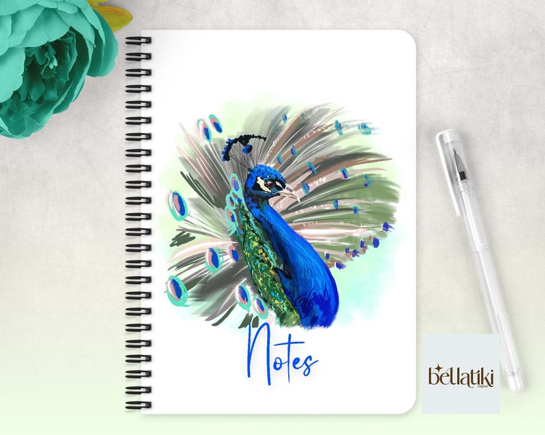 Peut inclure: Un carnet &agrave; spirales avec une couverture blanche illustrant un paon color&eacute; d&eacute;ployant ses plumes. Le texte "Notes" est imprim&eacute; en bleu sous le paon. La marque "bellatiki" est imprim&eacute;e en bas &agrave; droite.