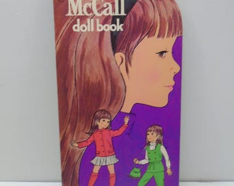 May include: A vintage Betsy McCall doll book featuring a large illustration of a girl with long brown hair on a purple background. The cover displays two smaller figures of the same character wearing a red jacket with a skirt and a green outfit.