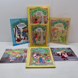 Puede incluir: Una colección de libros y libros para colorear de Cabbage Patch Kids. Los libros tienen cubiertas amarillas con títulos como "Xavier's Fantastic Discovery" y "The Shortest Route in the Patch". El libro para colorear es azul y presenta un Cabbage Patch Kid pintando.