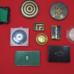 Op de afbeelding: Assortiment van vintage compact spiegels met verschillende ontwerpen. De spiegels zijn gemaakt van metaal en hebben verschillende kleuren en patronen, waaronder groen, blauw, goud en zwart.