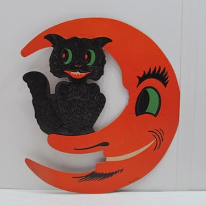 May include: A vintage Halloween decoration featuring a black cat sitting on a crescent moon with a smiling face. The moon is orange and the cat has green eyes.